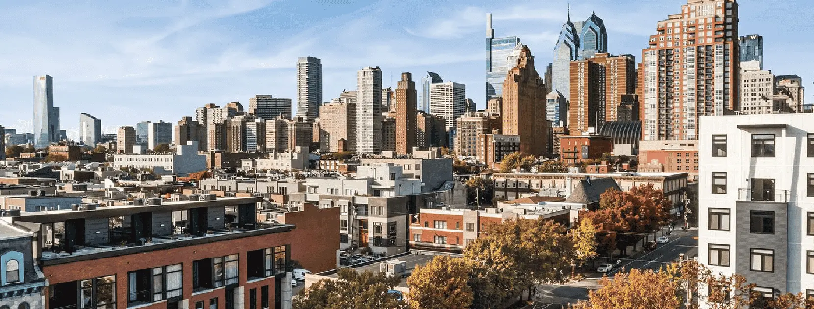 Graduate Hospital neighborhood featuring historic row homes, modern townhouses, leafy sidewalks, and people walking or biking along the bustling, tree-lined street.