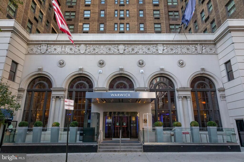 Entrance of The Warwick Condominiums in Philadelphia, featuring a historic brick façade with arched windows, decorative stone detailing, and a modern canopy labeled “Warwick.”