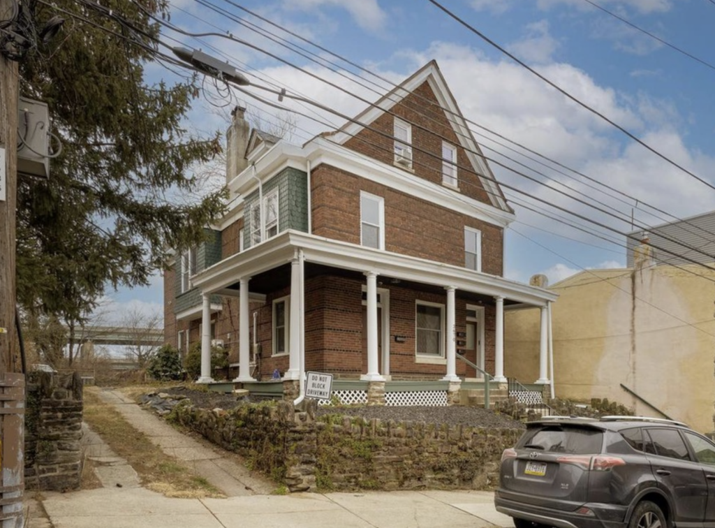 Large brick multi-unit home in East Falls with a covered front porch, white columns, and a corner lot. The property features multiple entrances and off-street parking along the side driveway.