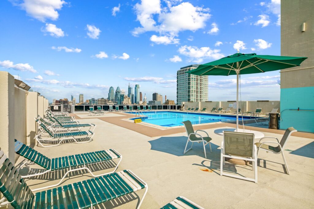 Hopkinson House rooftop pool deck featuring lounge chairs, umbrella seating, and sweeping views of the Philadelphia skyline.
